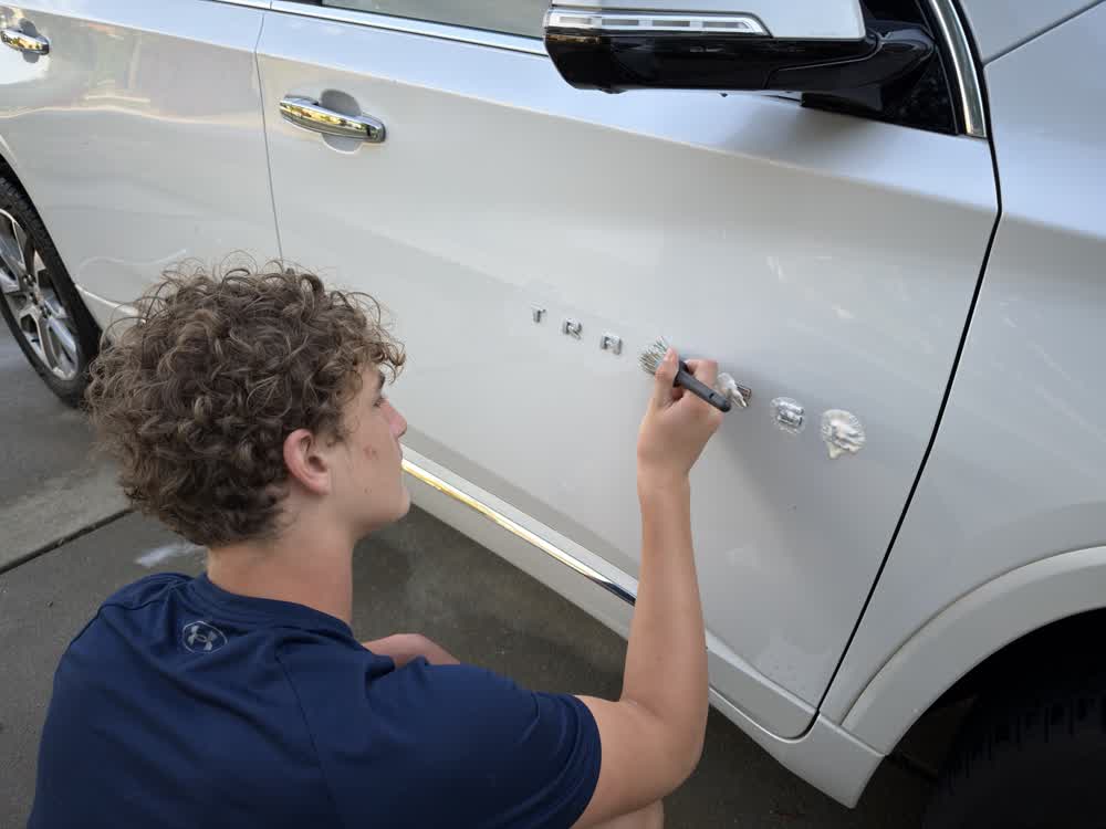 Charlie using a soft brush and compound to clean around emblems on the side of a white SUV
